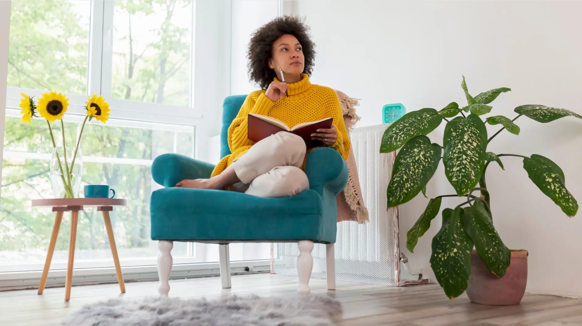 A woman lost in thought while sitting on a comfy blue couch with a notebook in her lap and a pencil in her hand