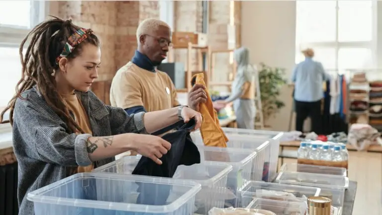 A man and woman volunteering by organizing clothes for a non-profit into different bins on a table