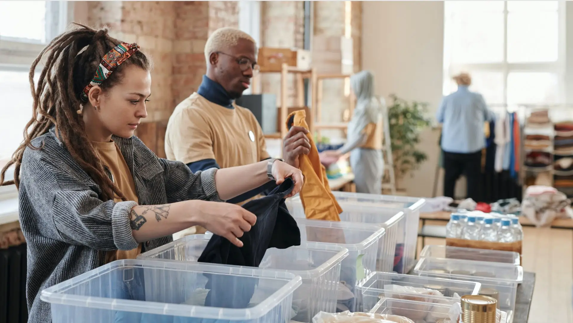 A man and woman volunteering by organizing clothes for a non-profit into different bins on a table