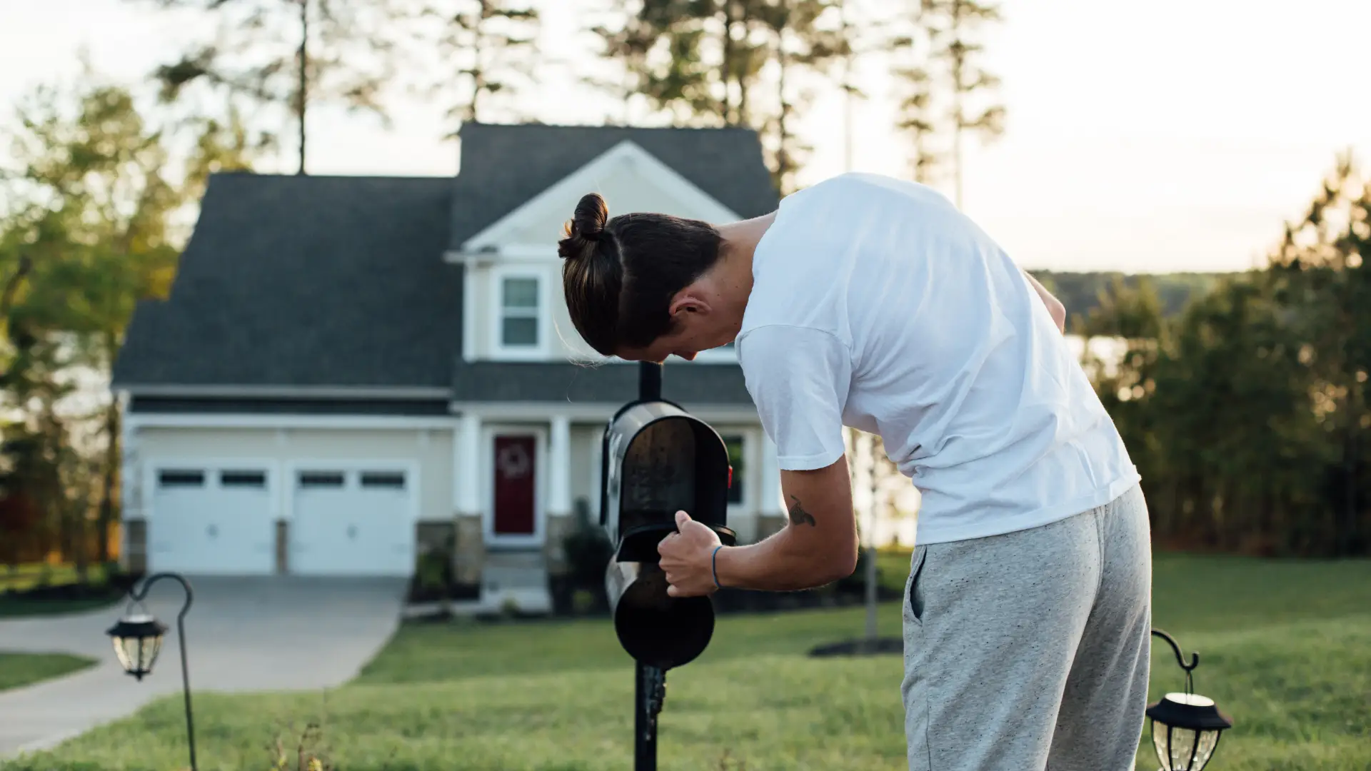 Man checking mailbox in front of house in white t-shirt and grey sweatpants