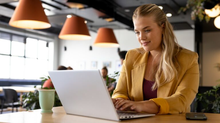 A woman working from a restaurant on her laptop with a cup of coffee or tea next to her