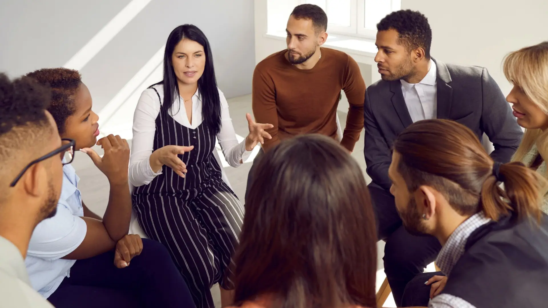 A woman surrounded by people leaning in to hear her tell a story, presumably in an office setting