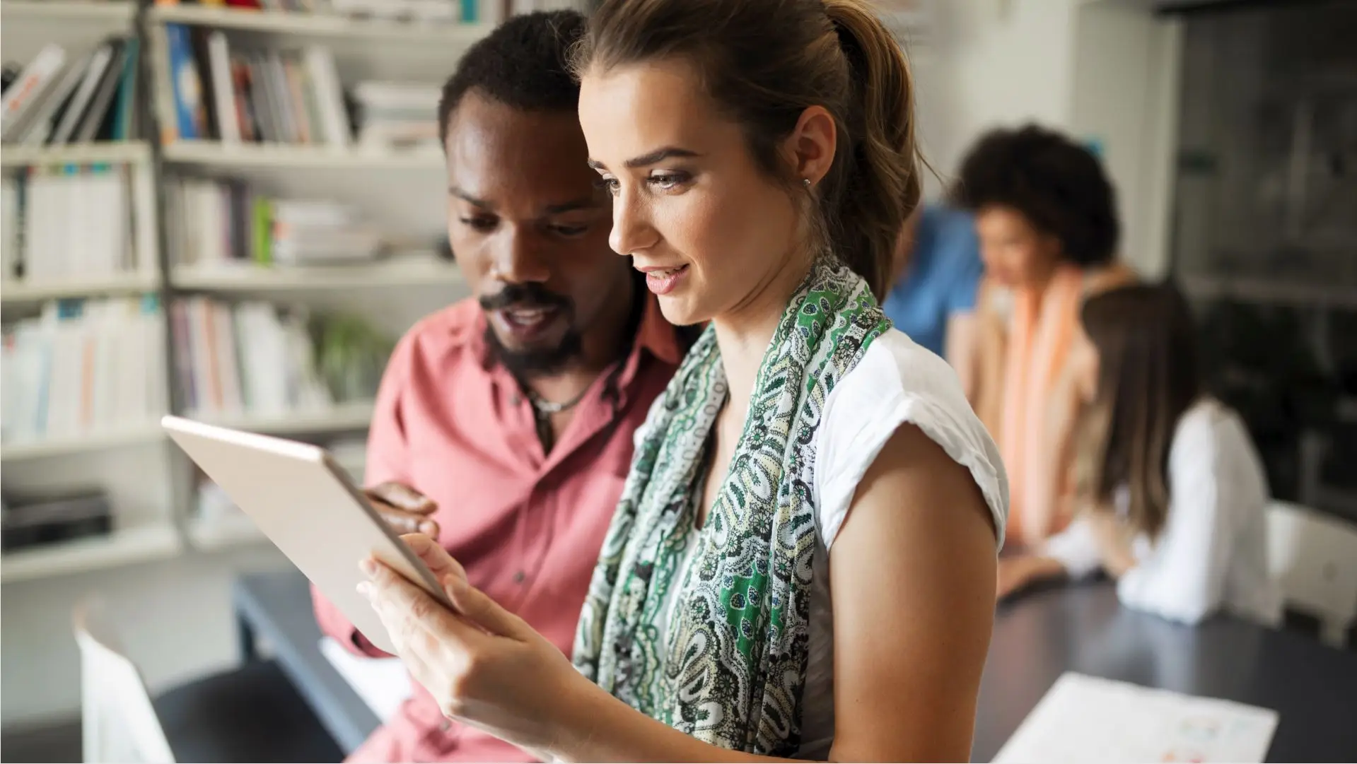 A woman reviewing something on a tablet, while a man stands next to her pointing to a part of the screen, presumably they're working together as a team