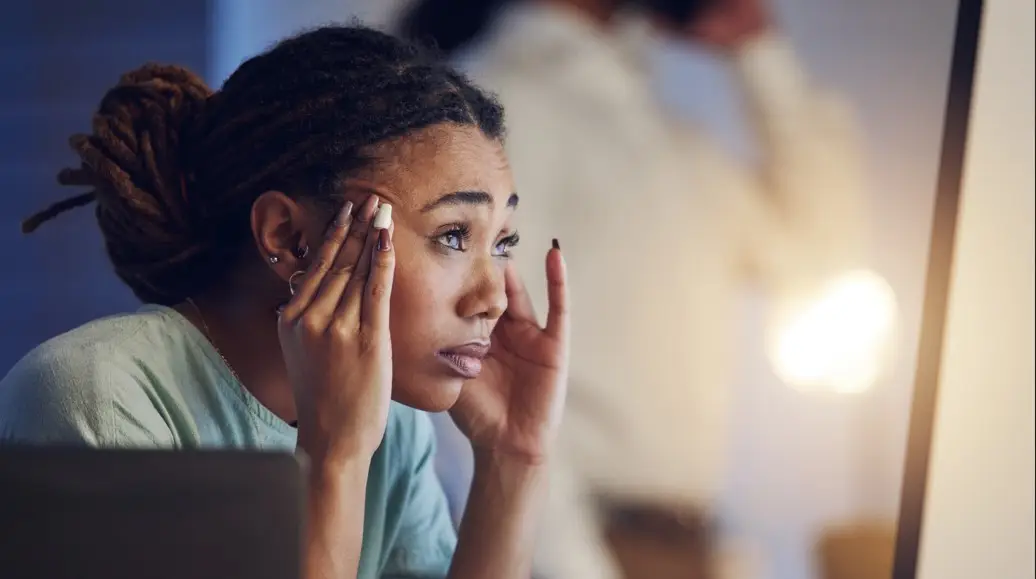 A woman rubbing her temples while staring at a computer screen