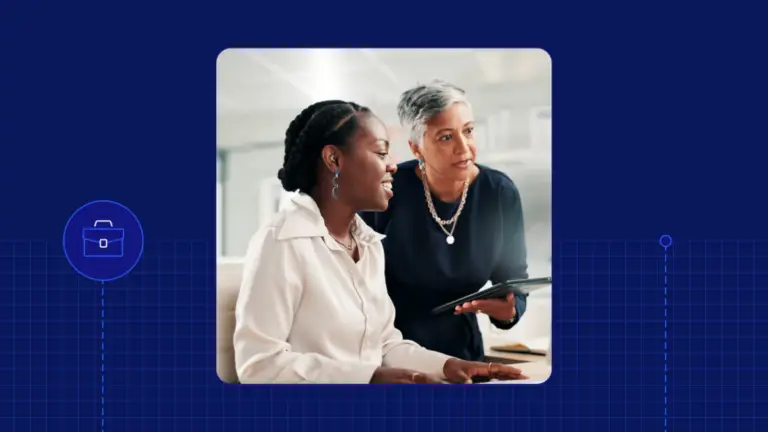 Two women in a professional setting, one holding a tablet and speaking while the other listens attentively, both smiling.
