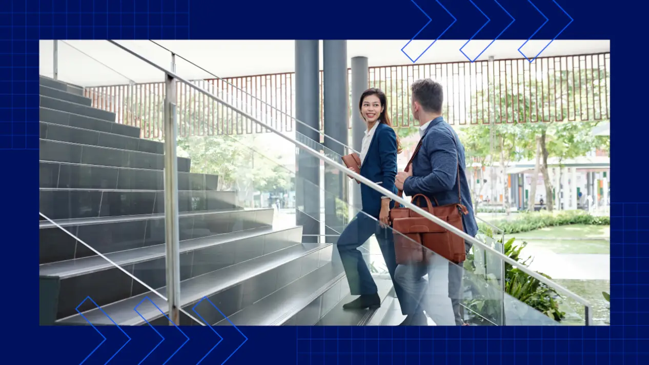 Two professionally dressed people walk up a staircase inside a modern office building.